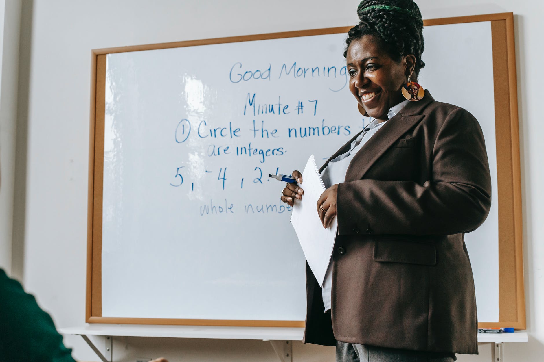 crop cheerful black female teacher standing near whiteboard in classroom